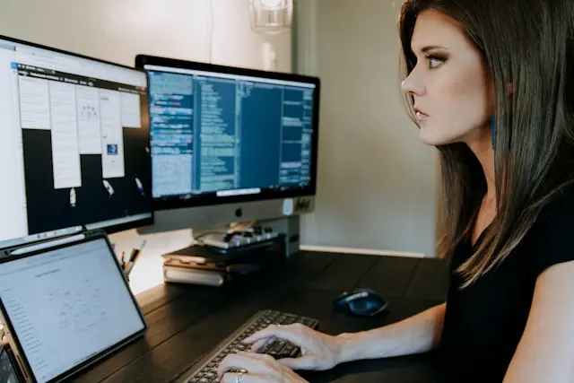 mujer frente a una laptop y dos monitores